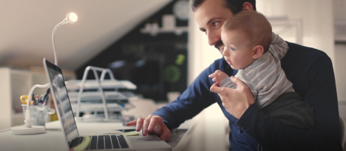 Dad working on laptop while holding a baby