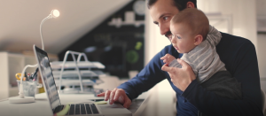 Dad working on laptop while holding a baby